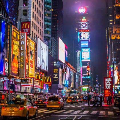 Times Square at night with towering illuminated billboards and busy street traffic.